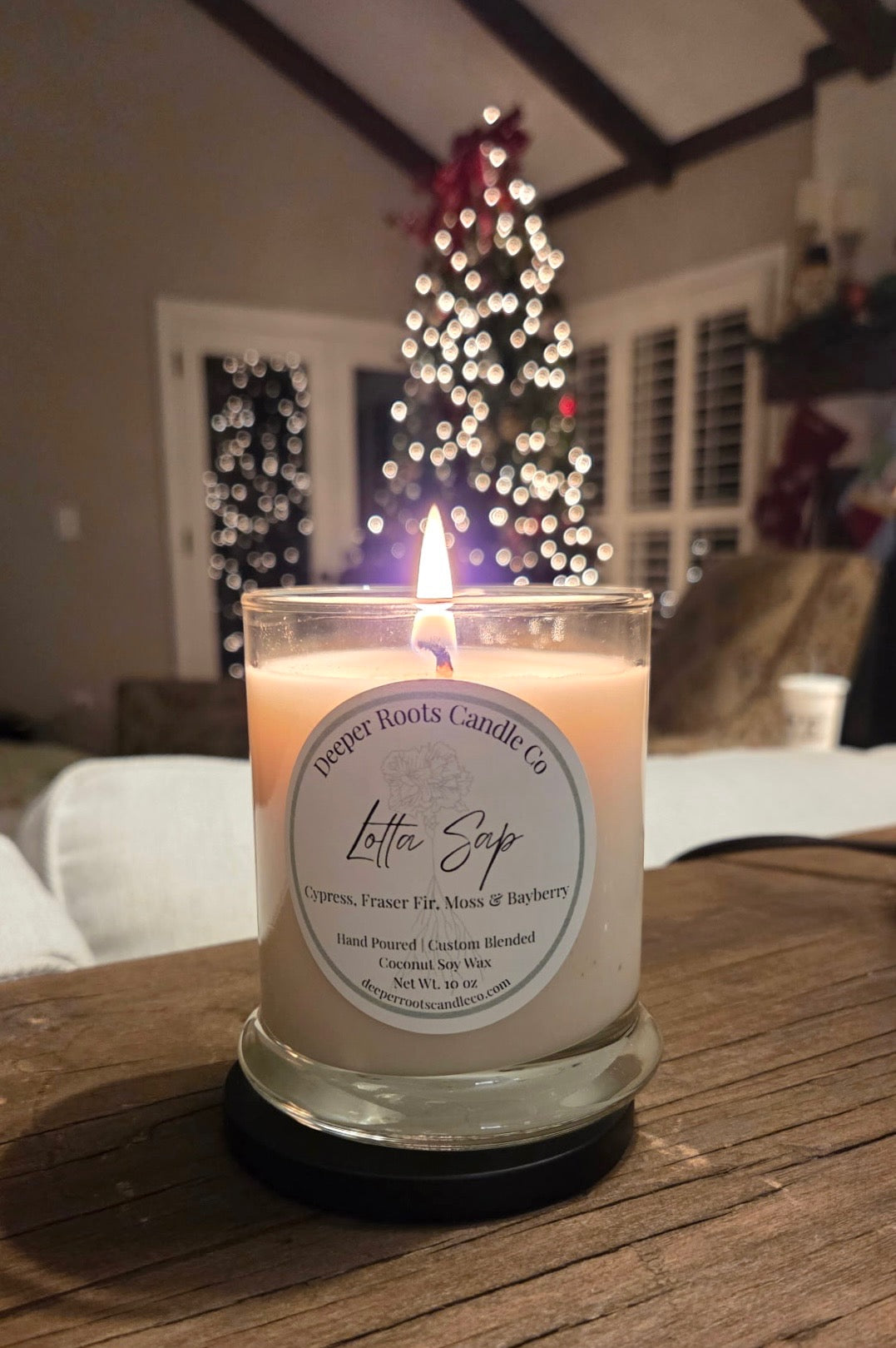 Lit Lotta Sap candle on a table with a Christmas tree in the background